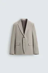 Blazer slim fit de color beige, confeccionada en tejido con lana. Presenta cuello con solapas de muesca, cierre frontal con un botón, bolsillos con solapa en la cadera y bolsillo de vivo en el pecho.
