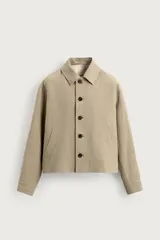 Sobrecamisa cropped fit de lino color beige, con cuello solapa, mangas largas con puño abotonado, bolsillos frontales de vivo y cierre frontal con botones oscuros.