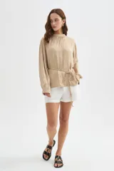 Blusa de poliéster color negro con cuello alto, mangas largas, diseño holgado, detalles de frunces y lazo ajustable en la cintura.