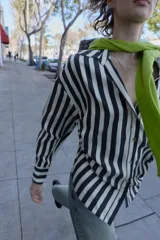 Camisa de cuello solapa con escote pico y manga larga. Presenta un bolsillo delantero de plastrón y bajo con aberturas laterales con cordones ajustables. Cierre frontal con botones.