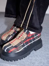 Mocasines con plataforma de goma negra, confeccionados en lona con estampa a cuadros en tonos violeta, amarillo y beige, y detalle de elásticos laterales ocultos.