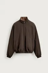 Cazadora bomber reversible de corte relaxed fit, color marrón oscuro, con cuello alto, cierre frontal de cremallera, bolsillos laterales de vivo y acabados elásticos en puños y dobladillo.