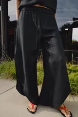 Pantalón de tiro medio confeccionado en lino, con cintura elástica ajustable mediante cordones. Presenta un diseño de pernera ancha con bajo redondeado y aberturas laterales.