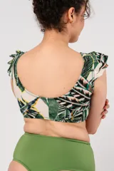 Top de bikini con estampado de hojas de palmera en tonos verde, blanco y amarillo. Tiene volados en los hombros, nudo en el escote y bolsillo interno para colocar copa removible o prótesis externa.