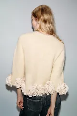 Jersey de punto color crema con cuello redondo y mangas tres cuartos. Presenta un diseño holgado con el ruedo decorado con aplicaciones de flores de tela en relieve.