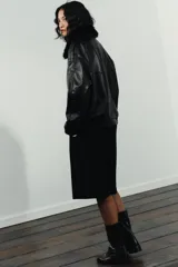 Cazadora de cuero sintético en color negro, con cuello de solapa y aplicación de pelo sintético desmontable. Presenta cierre frontal con cremallera y botones a presión ocultos, bolsillos de plastrón con solapa en el delantero y bajo con elástico.