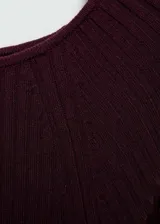 Vestido midi de punto acanalado en color bordó, con cuello barco, manga larga y diseño entallado. Incluye un cinturón desmontable de la misma tela para ajustar a la cintura y presenta una abertura lateral.