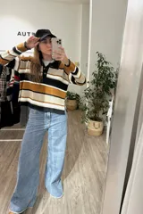 Sweater de punto con diseño a rayas horizontales en tonos negro, beige y mostaza. Presenta cuello tipo polo con cierre de botones, mangas largas y corte holgado.