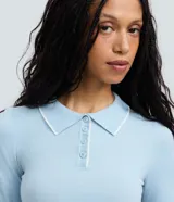 Blusa de punto manga larga con cuello polo y cierre frontal de botones. Presenta un diseño ajustado al cuerpo con detalles de ribetes en color blanco en el cuello, puños y ruedo.