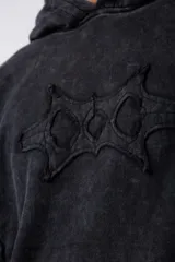 Buzo canguro de corte oversize, confeccionado en frisa de algodón con efecto de lavado gastado. Presenta un aplique decorativo cosido al corte en el centro del pecho, capucha amplia y bolsillo frontal tipo canguro.