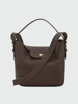 Cartera bucket de cuero marrón texturizado, con solapa frontal con cierre de botón a presión metálico dorado, asa corta superior y correa cruzada ajustable.