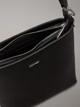 Cartera tipo saco pequeña Calvin Klein color negro, de cuero sintético granulado. Tiene dos correas desmontables: una correa fina ajustable y una correa ancha ajustable con logo jacquard.