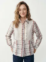 Camisa de algodón a cuadros en tonos vino, piedra y crudo, con pechera frontal decorada con puntillas y volados. Presenta cuello clásico, cierre frontal con botones y mangas largas con volumen sutil.