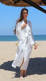 Kimono largo de color blanco con textura sutil, diseño holgado, mangas anchas y lazo ajustable en la cintura. Presenta un aplique decorativo en la espalda.