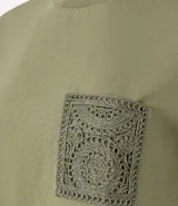 Remera de manga corta y cuello redondo color verde oliva, confeccionada en algodón, con un bolsillo cuadrado aplicado en el pecho con diseño de crochet intrincado.