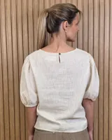 Blusa blanca de lino, con cuello redondo y mangas cortas abullonadas con frunces en los hombros.