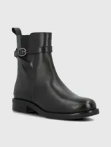 Bota corta de cuero negro con punta redonda, cierre lateral y detalle de tira con hebilla metálica en el tobillo.