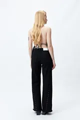 Pantalón de denim corte wide leg color marrón, con ruedo desflecado y detalle de tachas metálicas a lo largo de las costuras laterales.