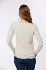 Buzo tejido en hilo de algodón color beige, con cuello redondo y manga larga. Presenta un corte clásico y un pequeño detalle metálico en la parte inferior izquierda.