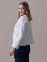 Chaqueta Nanette de tejido tweed color blanco, con escote mao, abertura central y bolsillos delanteros. Presenta apliques de botones perlados en los puños y terminación desflecada.