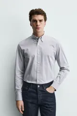 Camisa de corte regular fit confeccionada en tejido de algodón con estampado de microcuadros. Presenta cuello abotonado, manga larga con puños abotonados y cierre frontal de botones.