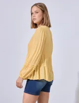 Blusa blanca de gasa con escote en V y apliques de puntilla en el frente. Manga larga con puño elastizado.