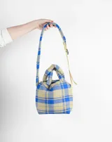 Bolso tipo tote bag con estampado a cuadros en tonos azul, beige y gris. Tiene doble asa corta y correa larga ajustable.