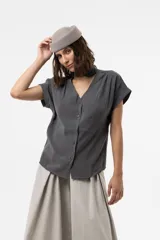 Camisa gris de corte relajado, con escote en V y lazo largo incorporado en el cuello. Mangas cortas con vuelta y frunce sutil en los hombros.
