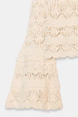 Jersey de punto color crema, con cuello redondo y manga larga acampanada. El tejido presenta un calado con patrón de rombos.
