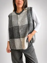 Chaleco de punto con diseño de cuadros grandes en tonos grises y blanco. Presenta un corte oversize, cuello redondo y cierre frontal con botones.
