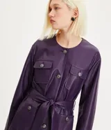 Campera alargada marca Cortelle confeccionada en poliuretano con textura que imita el cuero. Presenta cuello redondo, cierre frontal con botones metálicos, cuatro bolsillos delanteros con solapa y botones, y un lazo ajustable en la cintura.