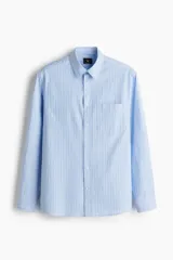 Camisa celeste y blanca a rayas verticales, de corte holgado, manga larga, cuello inglés, bolsillo en el pecho y cierre con botones.