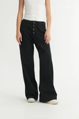 Pantalón de jean negro, de corte holgado desde la cadera hasta el bajo, con tiro medio y cierre frontal con botones.