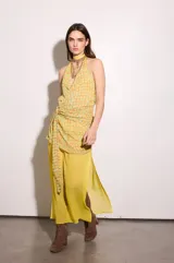 Vestido largo amarillo de gasa, con escote halter y estampado geométrico a cuadros. Cuenta con una capa superior cruzada atada a la cintura y falda larga fluida con aberturas laterales.