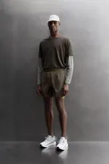 Short de running 2 en 1 color beige, confeccionado en tejido técnico ligero y elástico con malla interior integrada. Presenta cintura elástica ajustable con cordón, bolsillo trasero con cierre y aberturas laterales en el bajo.