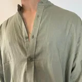 Camisa de manga larga en tejido de lino, color blanco, con cuello mao y cierre frontal de botones. Presenta un corte oversize y mangas con puños doblados.