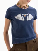 Remera de corte ajustado al cuerpo, color azul con efecto lavado, cuello redondo y mangas cortas. Presenta una estampa frontal de dos cisnes enfrentados y logo bordado en la espalda.