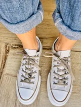 Zapatillas bajas de lona color blanco, con cordones marrones, puntera de goma y base blanca.