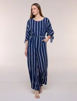 Enterito largo de crepe color azul marino con diseño de rayas verticales blancas. Cuenta con escote redondo, mangas tres cuartos con detalles de lazos en los puños, cintura elastizada con lazo extraíble para ajustar, bolsillos laterales y pantalón de corte amplio.