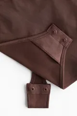 Body tanga de color marrón oscuro, con efecto vientre plano y copas forradas sin aros con sección en punto menguado para realzar el busto. Posee breteles ajustables y refuerzo interior con botones a presión ocultos.