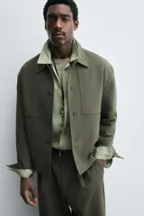 Sobrecamisa de corte boxy fit confeccionada en tejido compacto color beige, con cuello solapa, cierre frontal de botones y bolsillos laterales en costura.