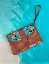Sobre de mano de cuero color marrón, con solapa y arte pintado a mano en tonos celestes y naranjas, y correa de muñeca.