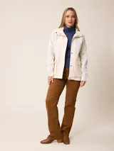 Campera de corte recto y estilo funcional, color beige, con capucha integrada, cierre frontal con botones a presión y bolsillos delanteros amplios. Presenta un diseño minimalista con cordones ajustables en la capucha.