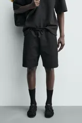 Bermuda estilo jogger de ajuste relajado, color negro, confeccionada en tejido interlock de algodón. Cuenta con cintura elástica ajustable mediante cordón, bolsillos delanteros tipo vivo y diseño liso.