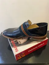 Mocasín de cuero color beige con textura reptil, detalle de tira ancha horizontal y suela de madera.