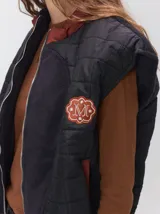 Chaleco de corte cuadrado con diseño bicolor en tonos terracota y crema. Presenta cierre frontal metalizado, parches de nylon en el pecho, interior forrado en corderito y cordón ajustable en el ruedo.