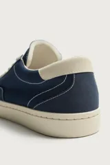 Zapatilla casual de tejido de algodón color beige con detalles en verde y un parche negro en el talón. Cuenta con suela de goma texturizada a contraste.