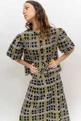 Camisa de popelina de algodón con cuello mao, botones frontales agrupados en pares y mangas cortas abullonadas tipo balloon. Cuenta con un diseño estampado de patrón geométrico y floral sobre fondo negro.