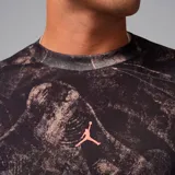 Camiseta de manga larga Jordan con cuello redondo y ajuste regular. Presenta un estampado tipo camuflaje abstracto en tonos oscuros con el logo Jumpman en color naranja en el centro del pecho.