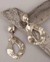 Par de aros colgantes de bronce y alpaca color plateado, con forma orgánica irregular y textura martillada. Cierre con perno y mariposa de plata 925.